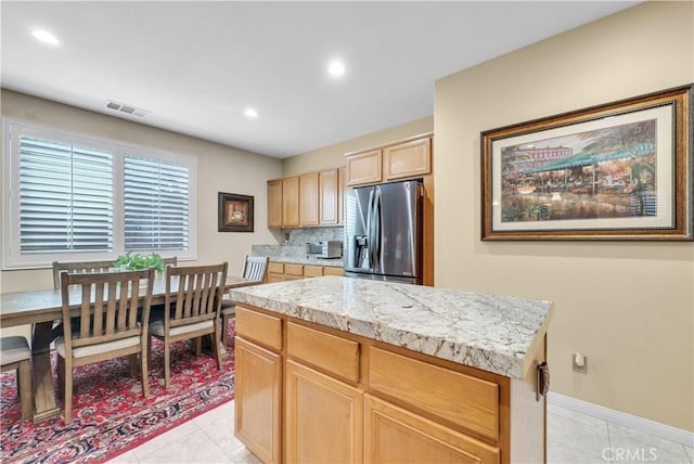 kitchen with light tile patterned floors, stainless steel refrigerator with ice dispenser, a kitchen island, and decorative backsplash