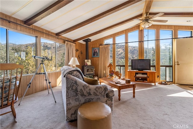 living room featuring ceiling fan, vaulted ceiling with beams, wood walls, a wood stove, and carpet