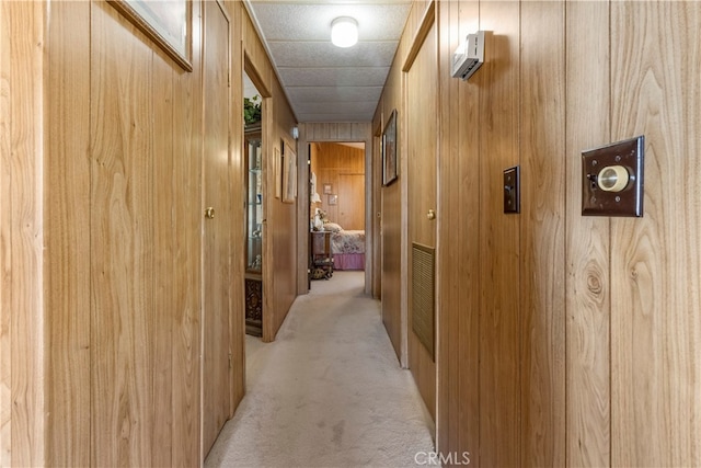 corridor featuring light carpet and wooden walls