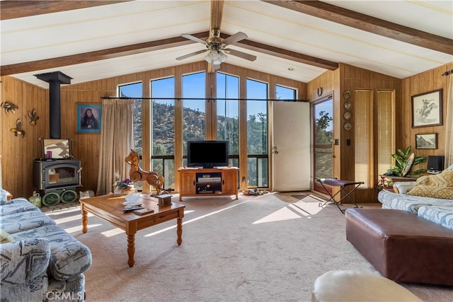 living room with wood walls, vaulted ceiling with beams, and a wood stove