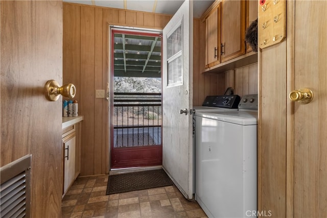 washroom with washing machine and dryer, wooden walls, and cabinets