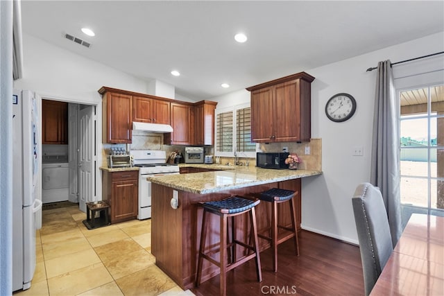 kitchen with kitchen peninsula, plenty of natural light, white appliances, and backsplash