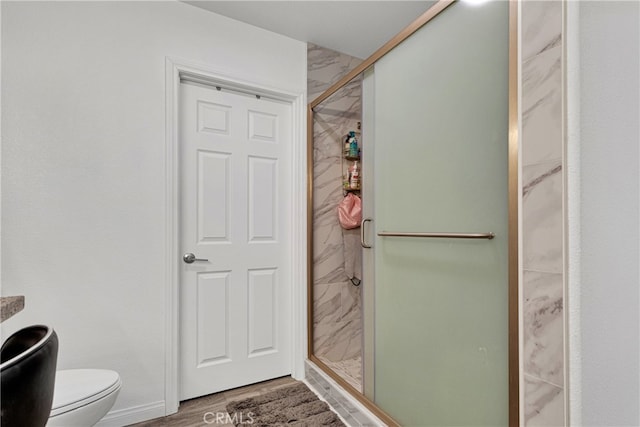 bathroom with hardwood / wood-style flooring, toilet, and a shower with door