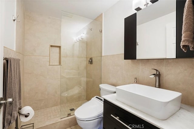 bathroom with a tile shower, vanity, toilet, and tile walls