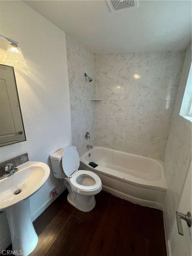 bathroom with tiled shower / bath combo, hardwood / wood-style flooring, and toilet