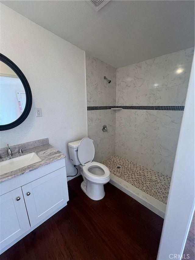 bathroom with a tile shower, toilet, vanity, and hardwood / wood-style flooring