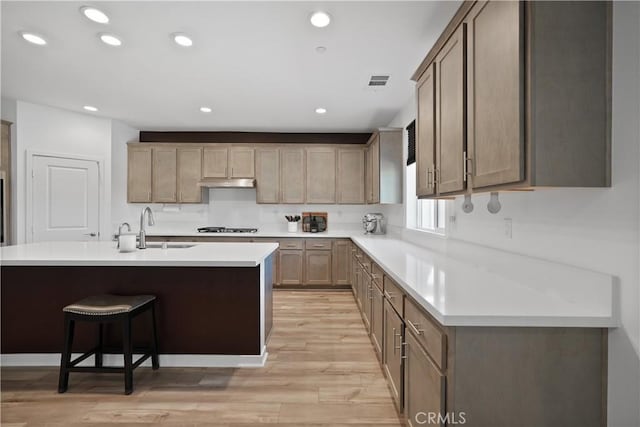 kitchen featuring light hardwood / wood-style floors, a kitchen island with sink, a kitchen breakfast bar, gas stovetop, and sink