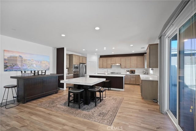 kitchen with a kitchen breakfast bar, appliances with stainless steel finishes, light hardwood / wood-style flooring, and a center island