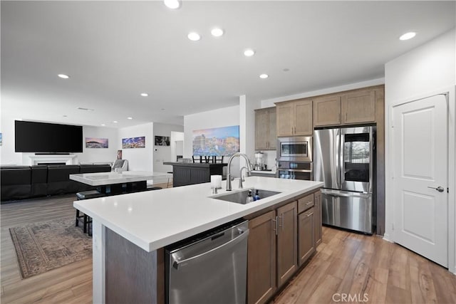 kitchen featuring sink, appliances with stainless steel finishes, light wood-type flooring, and an island with sink