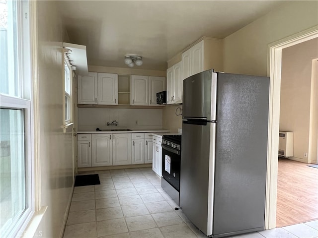 kitchen with sink, black appliances, light hardwood / wood-style flooring, and white cabinetry