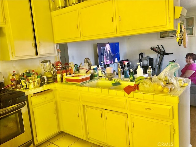 kitchen with tile counters, light tile patterned flooring, kitchen peninsula, and electric range oven