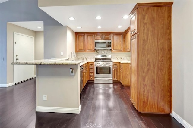 kitchen with appliances with stainless steel finishes, kitchen peninsula, light stone countertops, and dark hardwood / wood-style flooring