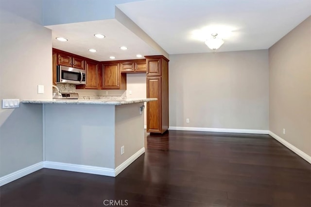 kitchen featuring light stone counters, appliances with stainless steel finishes, dark wood-type flooring, and kitchen peninsula