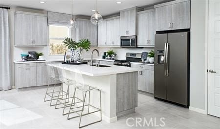 kitchen with a breakfast bar, a center island with sink, sink, stainless steel appliances, and hanging light fixtures