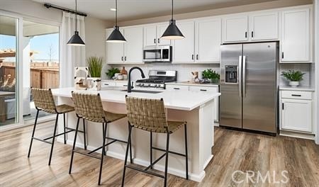 kitchen featuring wood-type flooring, a center island with sink, sink, stainless steel appliances, and white cabinets