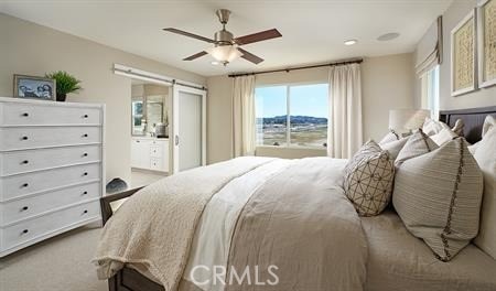 carpeted bedroom featuring ceiling fan, a barn door, and ensuite bathroom