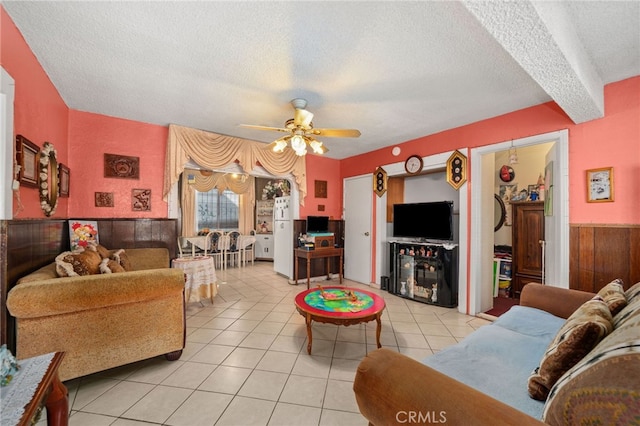 living room featuring ceiling fan, a textured ceiling, light tile patterned floors, and beam ceiling