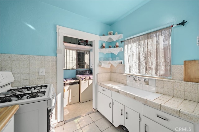 kitchen with washer and dryer, white gas range, white cabinetry, tile counters, and light tile patterned floors