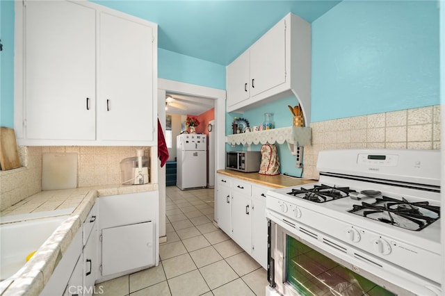 kitchen featuring white cabinets, tasteful backsplash, light tile patterned floors, sink, and white appliances