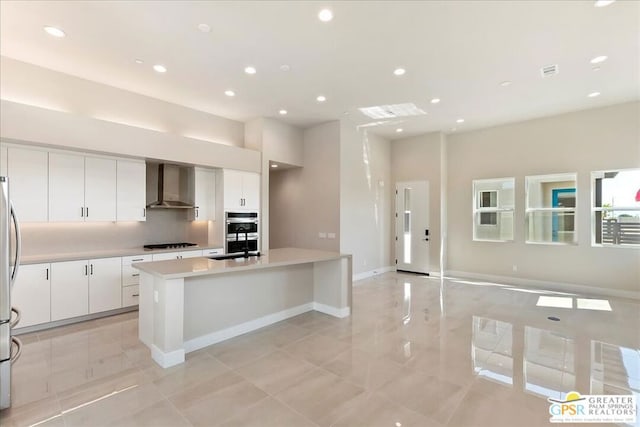 kitchen with white cabinets, a kitchen island with sink, wall chimney range hood, appliances with stainless steel finishes, and decorative backsplash