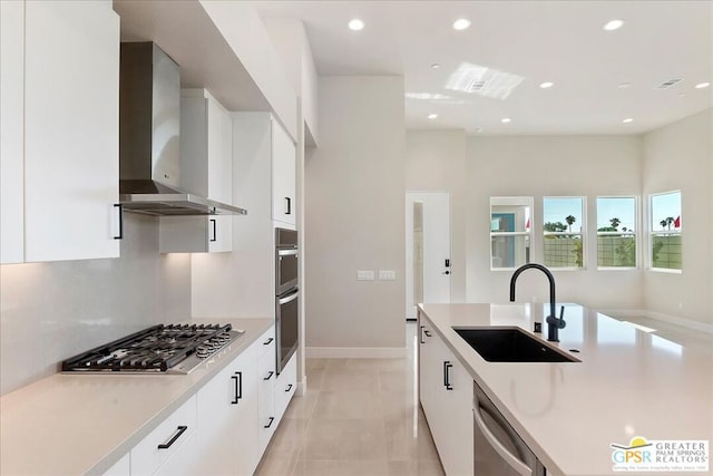 kitchen featuring appliances with stainless steel finishes, wall chimney exhaust hood, sink, and white cabinets