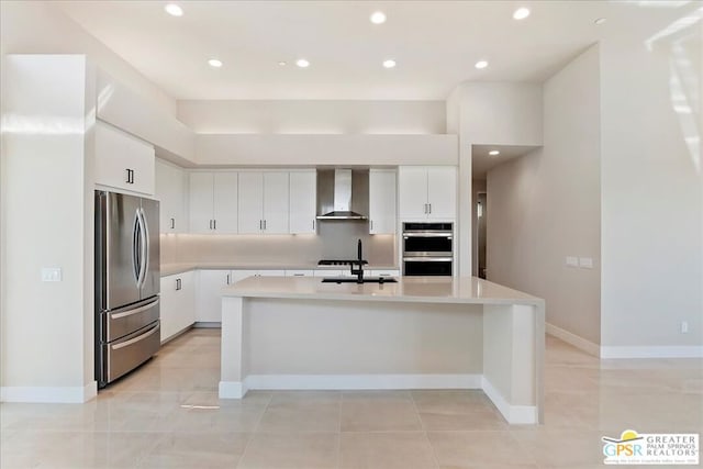 kitchen with sink, a kitchen island with sink, wall chimney range hood, white cabinetry, and appliances with stainless steel finishes