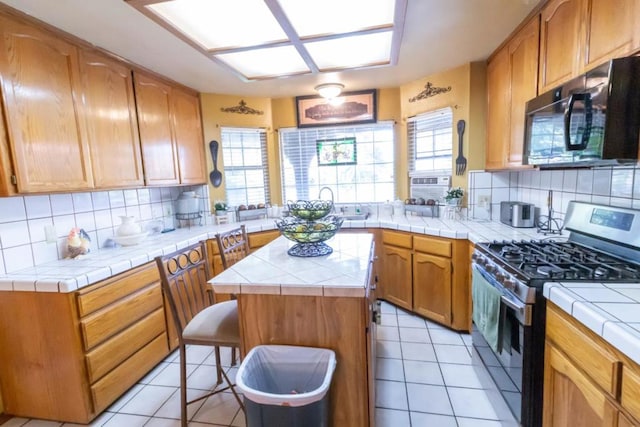 kitchen featuring decorative backsplash, tile counters, stainless steel gas range oven, and a kitchen island