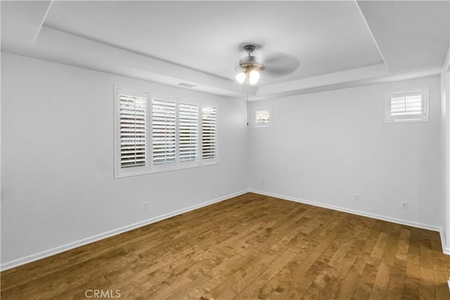 spare room featuring wood finished floors, a raised ceiling, a ceiling fan, and baseboards