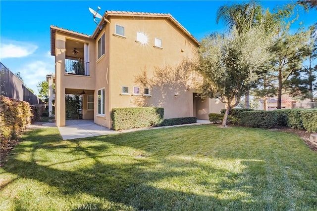 rear view of house with a patio area, a lawn, a balcony, and stucco siding