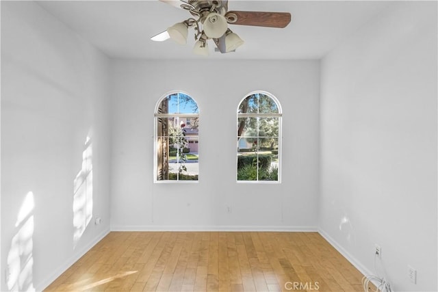 empty room with ceiling fan, light wood finished floors, and baseboards