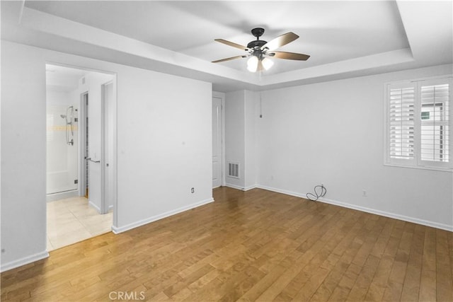 unfurnished room featuring ceiling fan, a raised ceiling, visible vents, and light wood-style floors