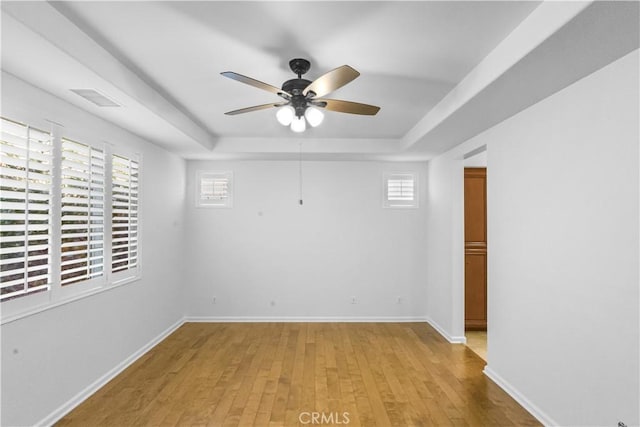 unfurnished room featuring a raised ceiling, visible vents, a ceiling fan, light wood-type flooring, and baseboards