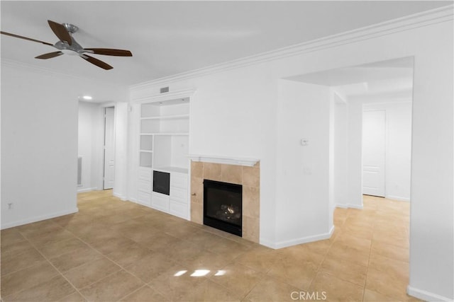 unfurnished living room with built in shelves, crown molding, a tiled fireplace, ceiling fan, and baseboards