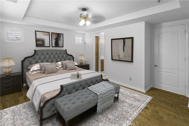 bedroom with ensuite bathroom, wood finished floors, a ceiling fan, baseboards, and a tray ceiling