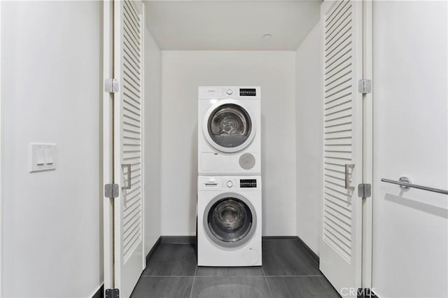 laundry room with dark tile patterned floors and stacked washer / drying machine