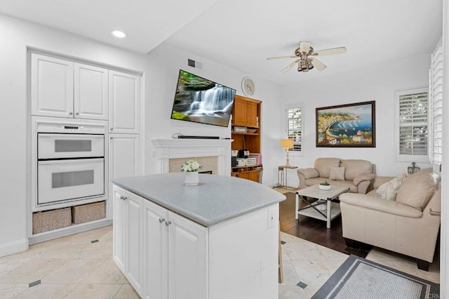 kitchen with ceiling fan, a center island, white cabinets, and white double oven