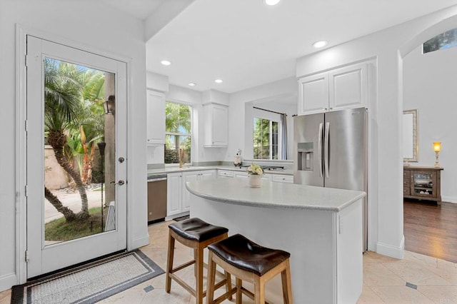 kitchen with light tile patterned flooring, a kitchen island, a breakfast bar, appliances with stainless steel finishes, and white cabinetry