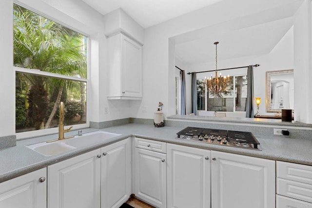 kitchen with pendant lighting, white cabinetry, sink, stainless steel gas cooktop, and a notable chandelier