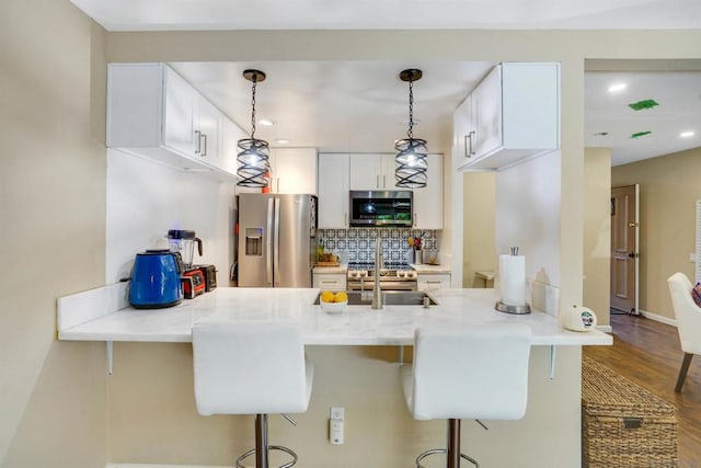 kitchen featuring hardwood / wood-style floors, stainless steel appliances, kitchen peninsula, pendant lighting, and white cabinetry