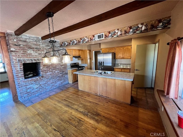 kitchen featuring stainless steel appliances, beamed ceiling, light hardwood / wood-style floors, hanging light fixtures, and a kitchen island with sink