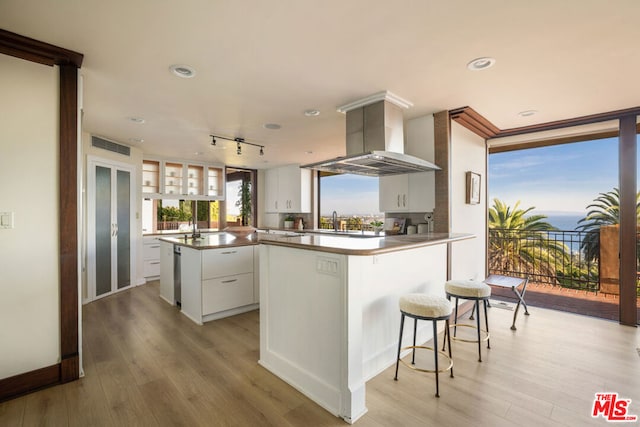 kitchen with wall chimney exhaust hood, light hardwood / wood-style floors, white cabinetry, and kitchen peninsula