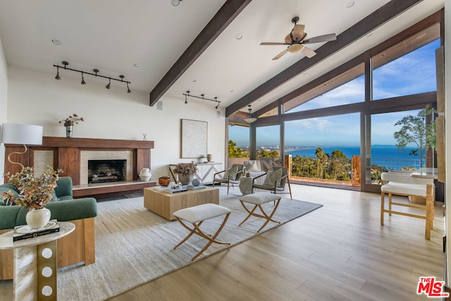 living room with rail lighting, ceiling fan, a water view, light hardwood / wood-style flooring, and vaulted ceiling with beams