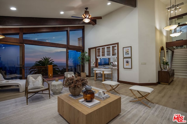 living room with beamed ceiling, ceiling fan with notable chandelier, light wood-type flooring, and high vaulted ceiling