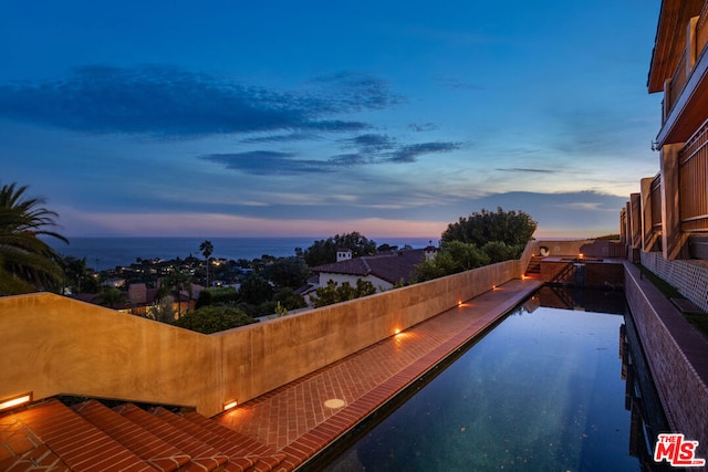 pool at dusk featuring a water view