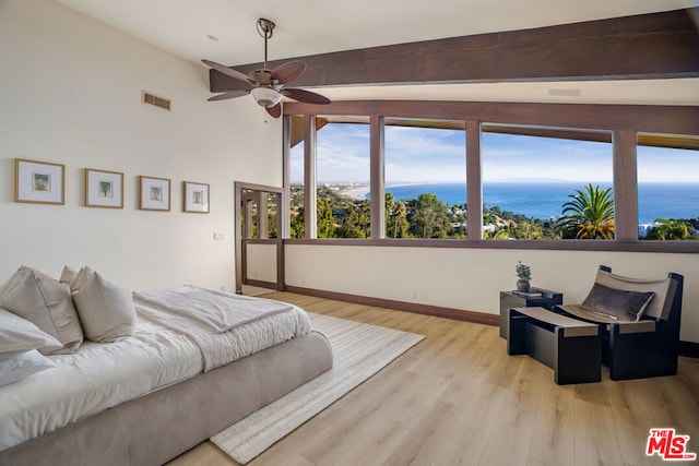 bedroom with lofted ceiling with beams, a water view, light hardwood / wood-style flooring, and ceiling fan