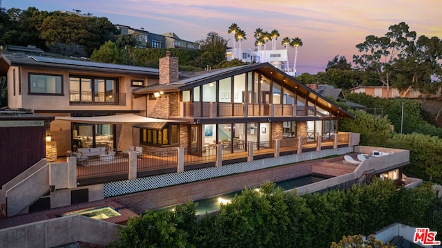 back house at dusk featuring an outdoor living space and a balcony