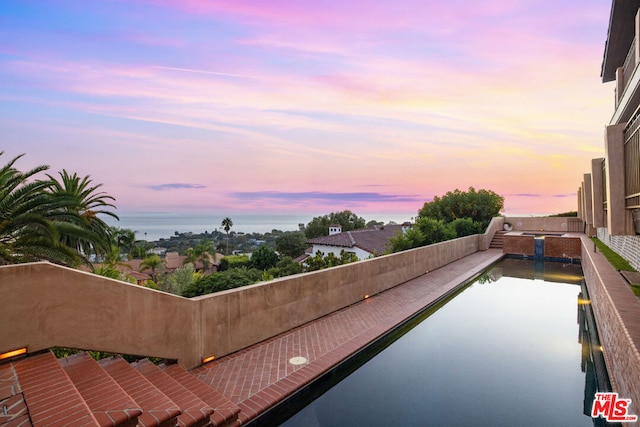 balcony at dusk featuring a water view