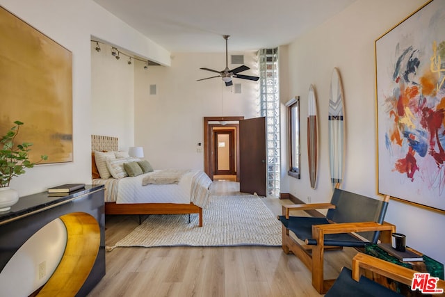 bedroom featuring ceiling fan, a towering ceiling, track lighting, and light wood-type flooring