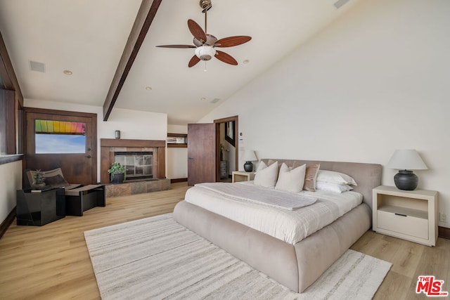 bedroom featuring light wood-type flooring, lofted ceiling with beams, ceiling fan, and a tiled fireplace