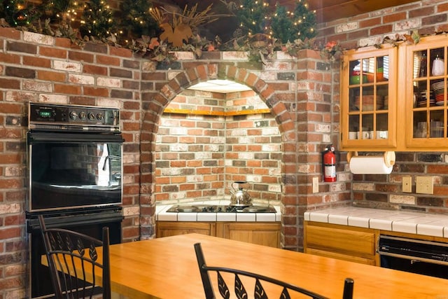 kitchen with tile counters, black appliances, and brick wall